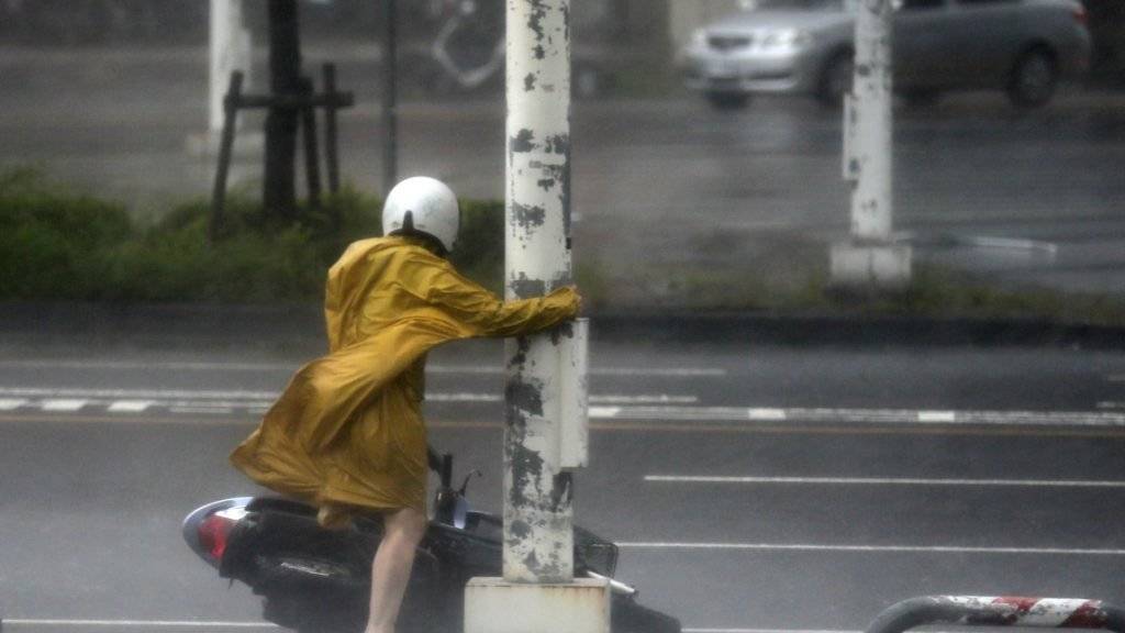 Eine Rollerfahrerin im Süden Taiwans hält sich wegen der starken Winde an einem Strassenpfosten fest.