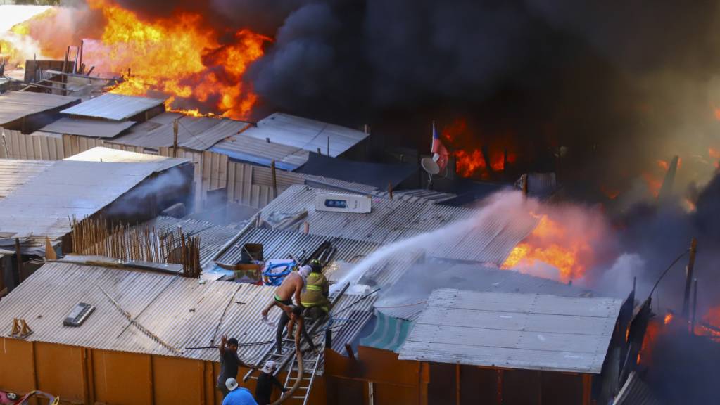 Nachbarn helfen Feuerwehrleuten bei der Bekämpfung eines Brandes in dem einkommensschwachen Viertel Laguna Verde in Iquique, im Norden von Chile. Bei dem Grossbrand sind mindestens 100 Häuser zerstört worden und mehr als 400 Menschen obdachlos geworden, teilte der Katastrophenschutz am Montag mit.