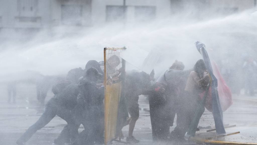 dpatopbilder - Demonstranten suchen Deckung, während die Polizei bei einer regierungskritischen Demonstration einen Wasserwerfer einsetzt, um sie auseinanderzutreiben. Foto: Rodrigo Abd/AP/dpa