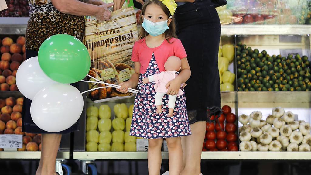 Ein Mädchen mit medizinischem Mundschutz hält Luftballons und eine Puppe in einem Lebensmittelmarkt in Bukarest. Rumänien verzeichnet einen Rekord an Neuinfektionen mit dem Coronavirus. Foto: Vadim Ghirda/AP/dpa
