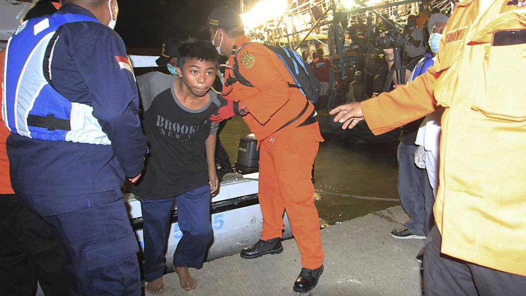 Rettungskräfte helfen einem der Überlebenden des Schiffsunglücks bei seiner Ankunft im Hafen von Indramayu. Foto: Panji Wisnu/AP/dpa