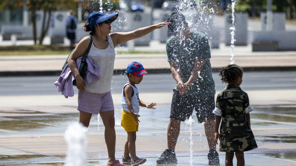 In Genf suchen Menschen bei der Hitze Abkühlung am Brunnen auf der Place des Nations.