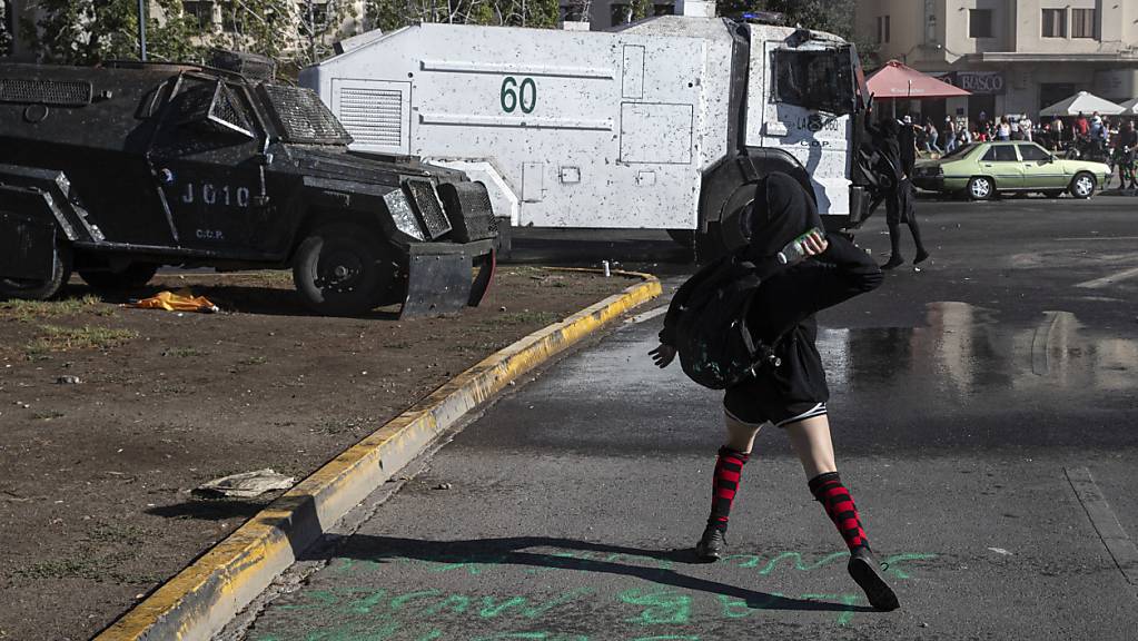 Eine Demonstrantin wirft eine Flasche auf einen Wasserwerfer der Polizei während einer Demonstration in Santiago de Chile am Internationalen Frauentag. Foto: Esteban Felix/AP/dpa