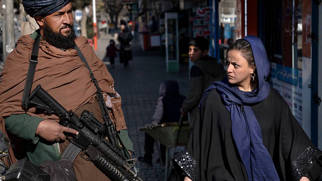ARCHIV - Ein Taliban-Kämpfer steht Wache während eine Frau vorbeiläuft. Foto: Ebrahim Noroozi/AP/dpa