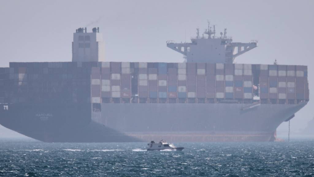 Ein Containerschiff liegt vor Anker, während im Vordergrund ein kleines Motorboot in der Straße von Hormus vor vorbeifährt. Foto: Amirhosein Khorgooi/ISNA/AP/dpa