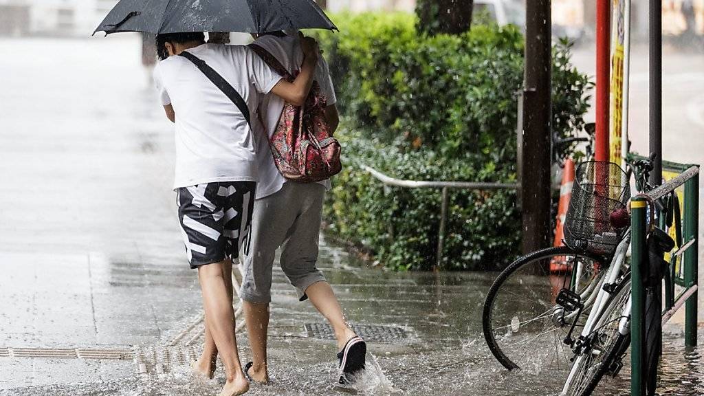 Zwei Fussgänger waten in Tokio durch eine teilweise überschwemmte Strasse.