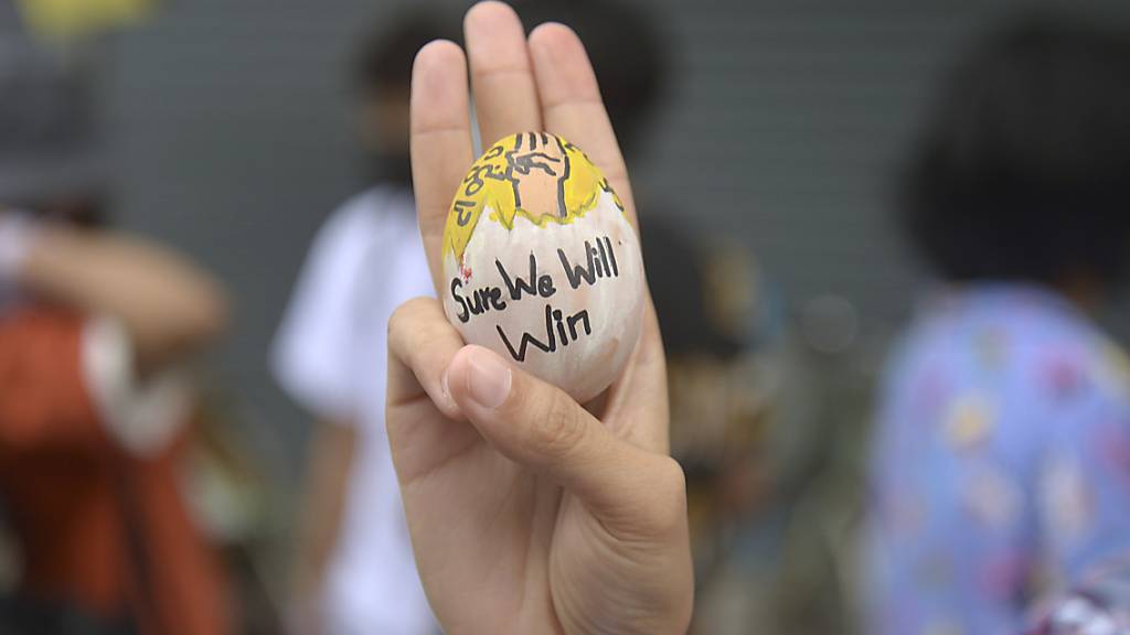 Ein Demonstrant zeigt den Drei-Finger-Gruß als Zeichen des Widerstands und hält dabei ein Osterei mit der Aufschrift «Sure we will win» (Wir werden sicher gewinnen) während eines Protestes gegen die Miltärjunta. Foto: Uncredited/AP/dpa