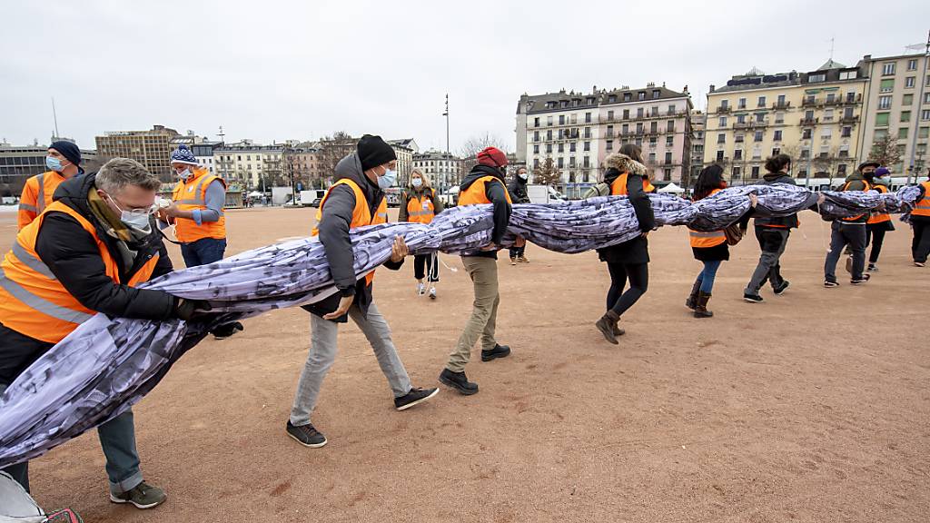 Freiwillige helfen mit die «We are watching»-Fahne in Genf zu entfalten. Quelle: KEYSTONE Fotograf: MARTIAL TREZZINI