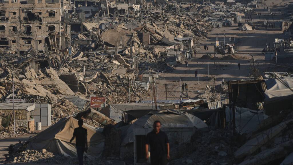 ARCHIV - Palästinenser gehen in Jabalia im Gazastreifen eine Straße entlang, die von Gebäuden gesäumt ist, die bei israelischen Militärangriffen während des Krieges zwischen Israel und der Hamas zerstört wurden. Foto: Jehad Alshrafi/AP/dpa