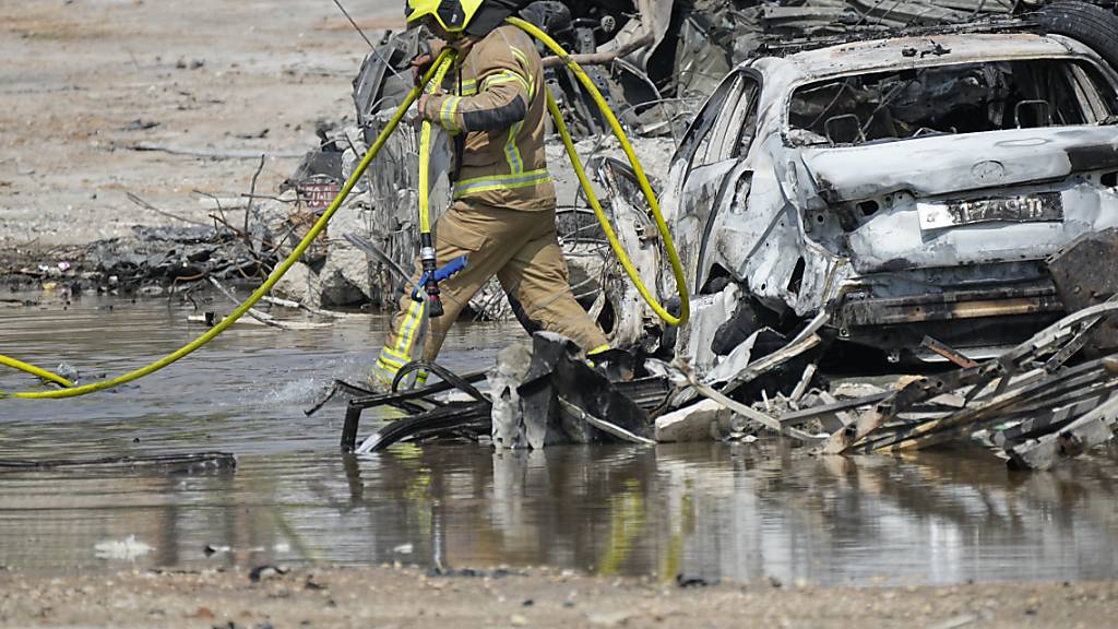 Ein israelischer Feuerwehrmann trägt einen Schlauch zu einer Polizeistation. Foto: Ohad Zwigenberg/AP/dpa