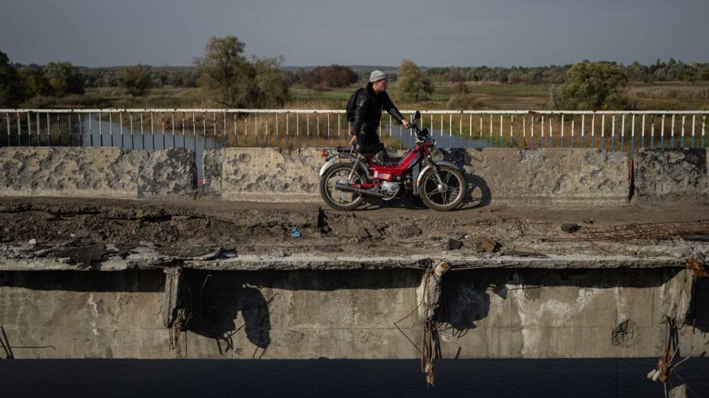 ARCHIV - Ein Mann zieht sein Motorrad auf einer zerstörten Brücke über den Fluss Oskil während einer Evakuierung in Kupjansk. Foto: Evgeniy Maloletka/AP/dpa