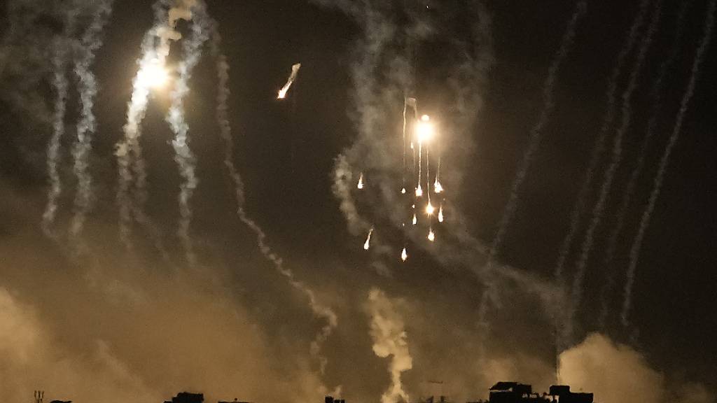 Rauch steigt während eines israelischen Luftangriffs im Gazastreifen auf und Leuchtraketen erhellen den Himmel, gesehen vom Süden Israels aus. Foto: Leo Correa/AP