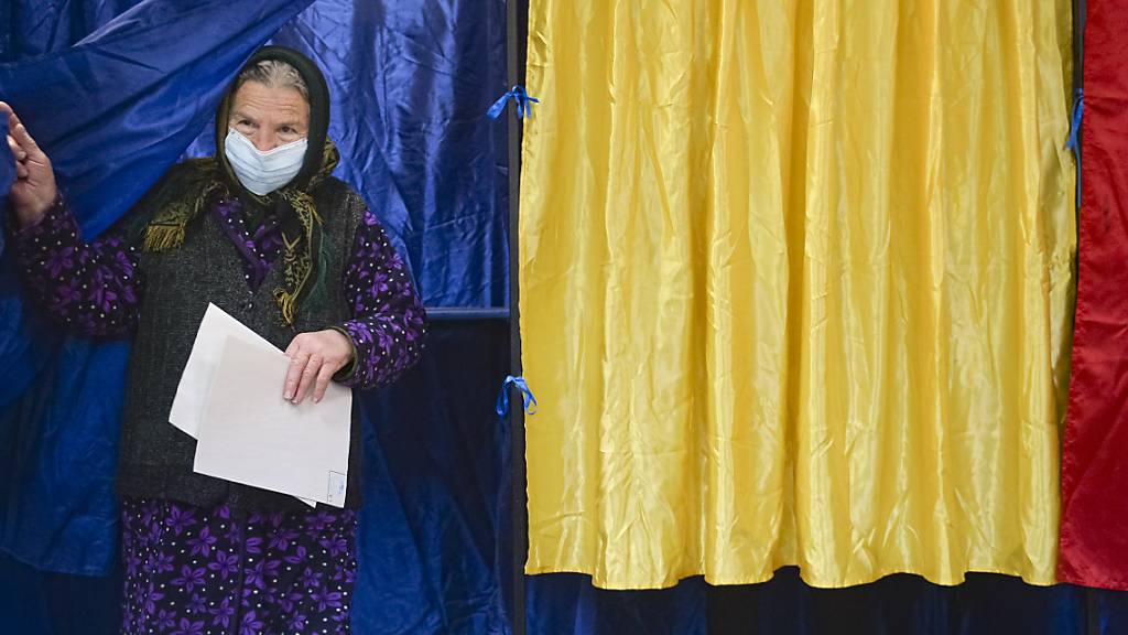 Eine Frau mit Mund-Nasen-Schutz verlässt eine Wahlkabine, nachdem sie bei den Parlamentswahlen ihre Wahlstimme abgegeben hat. Foto: Alexandru Dobre/AP/dpa