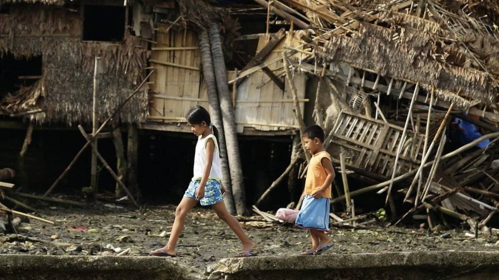 Kinder gehen über einen Deich, vor vom Taifun «Melor» zerstörten Häusern.