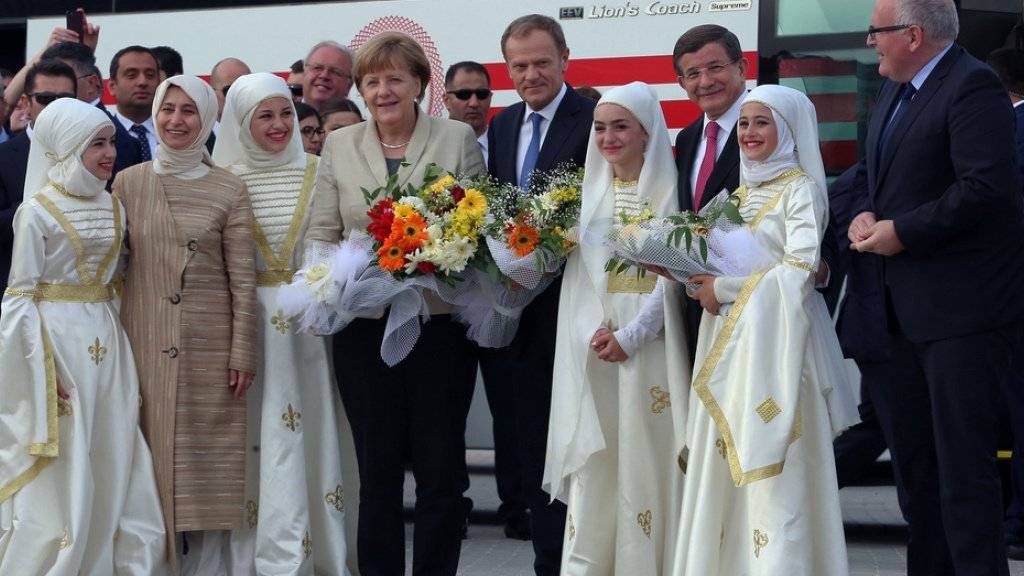 Angela Merkel, Donald Tusk, Ahmet Davutoglu und Frans Timmermans wurden von Flüchtlingen in traditioneller Tracht mit Blumen in Empfang genommen.