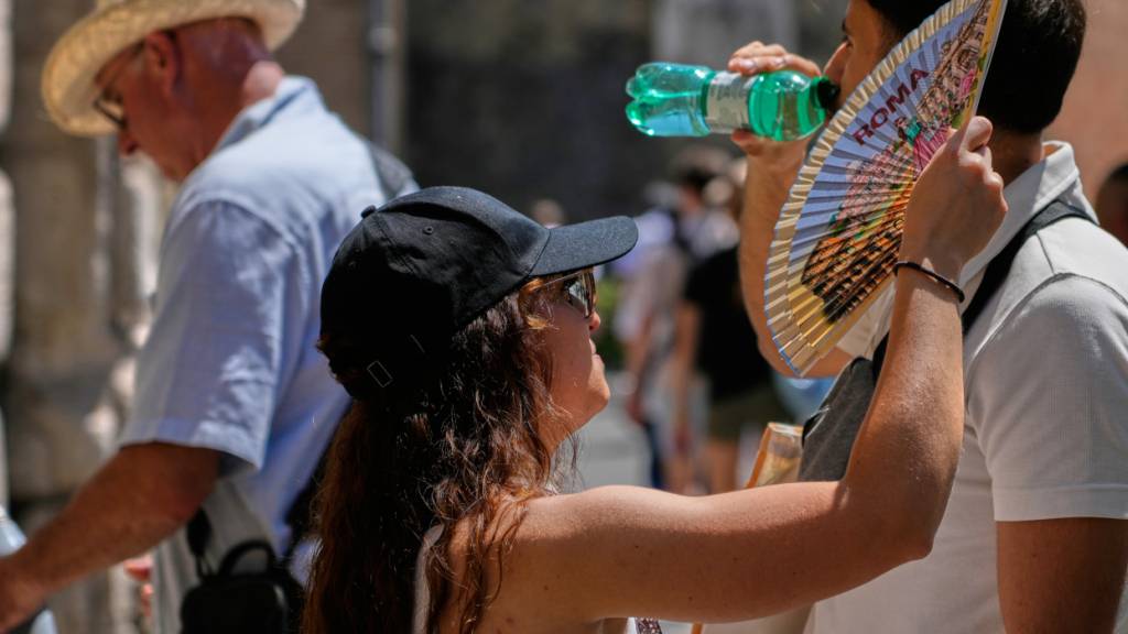 Eine Frau fächert sich Rom mit einem Fächer Luft zu, während ein Mann aus einer Wasserflasche trinkt. Foto: Gregorio Borgia/AP/dpa
