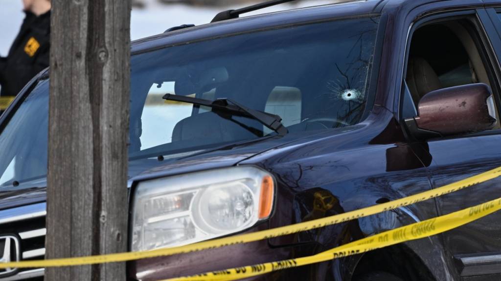 Ein Einschussloch ist in der Windschutzscheibe zu sehen, während Polizeibeamte am Tatort einer Schießerei arbeiten, in die Bundespolizisten verwickelt waren. Foto: Tom Baker/AP/dpa