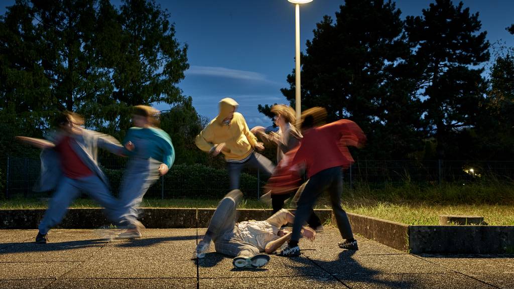 Symbolbild: Jugendliche treten in der Nacht auf ein Opfer am Boden ein.