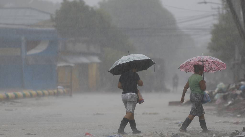 Zwei Frauen gehen bei starkem Regen über eine Straße. Rund zwei Wochen nach dem verheerenden Hurrikan «Eta» hat ein zweiter gefährlicher Sturm in Mittelamerika Land erreicht. Foto: Delmer Martinez/AP/dpa