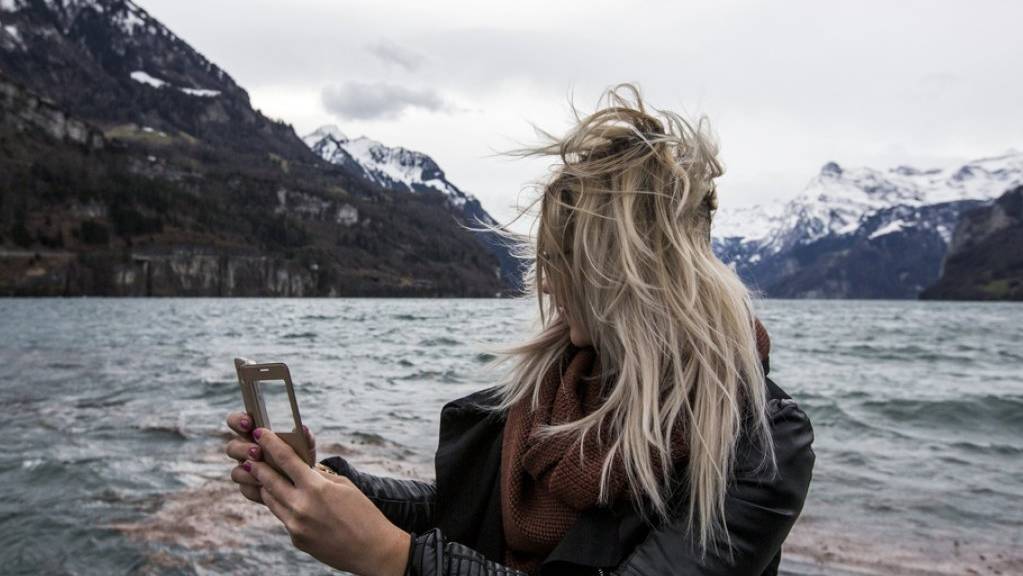 Frau mit verwehten Haaren am Urnersee mit einem Handy in den Händen