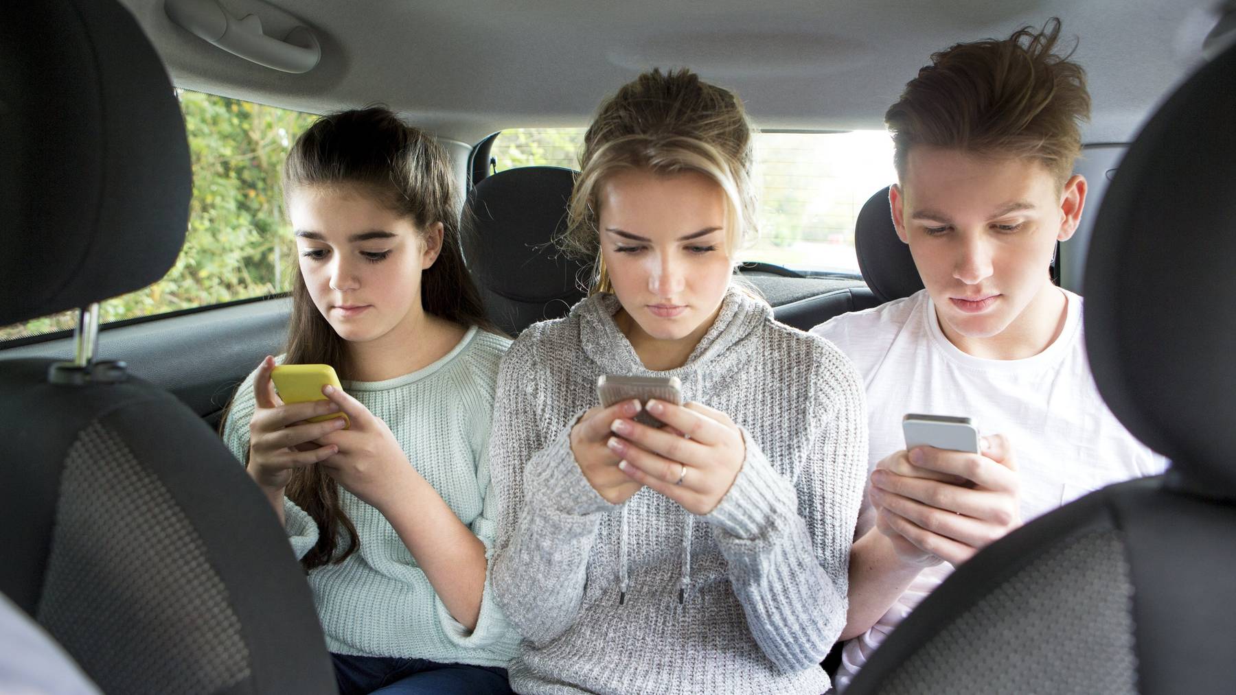 Diese Teenager haben nur Augen für ihr Smartphone –  dabei müssten sie sich anschnallen und, je nach Land, auf eine Erhöhung setzen. (Symbolbild)