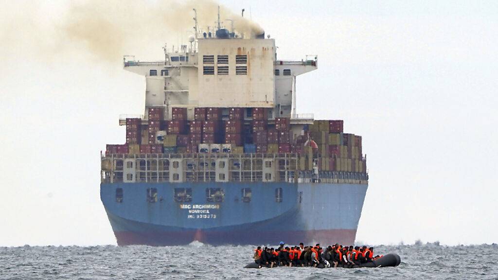 ARCHIV - Eine Gruppe von Menschen, bei denen es sich vermutlich um Migranten handelt, überquert den Ärmelkanal in einem kleinen Boot von der französischen Küste aus in Richtung Dover. Foto: Gareth Fuller/AP/dpa