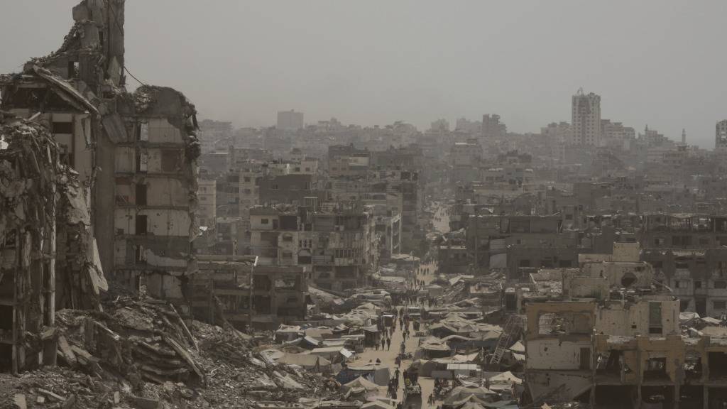 ARCHIV - Menschen gehen eine Straße entlang, die von Gebäuden umgeben ist, die durch israelische Bombardierungen im Gazastreifen zerstört wurden. Foto: Jehad Alshrafi/AP/dpa