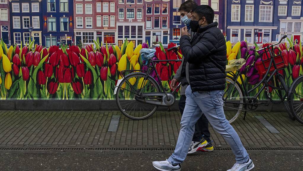 Passanten gehen an einer Wand, die mit Tulpen bemalt ist, vorbei. Foto: Peter Dejong/AP/dpa