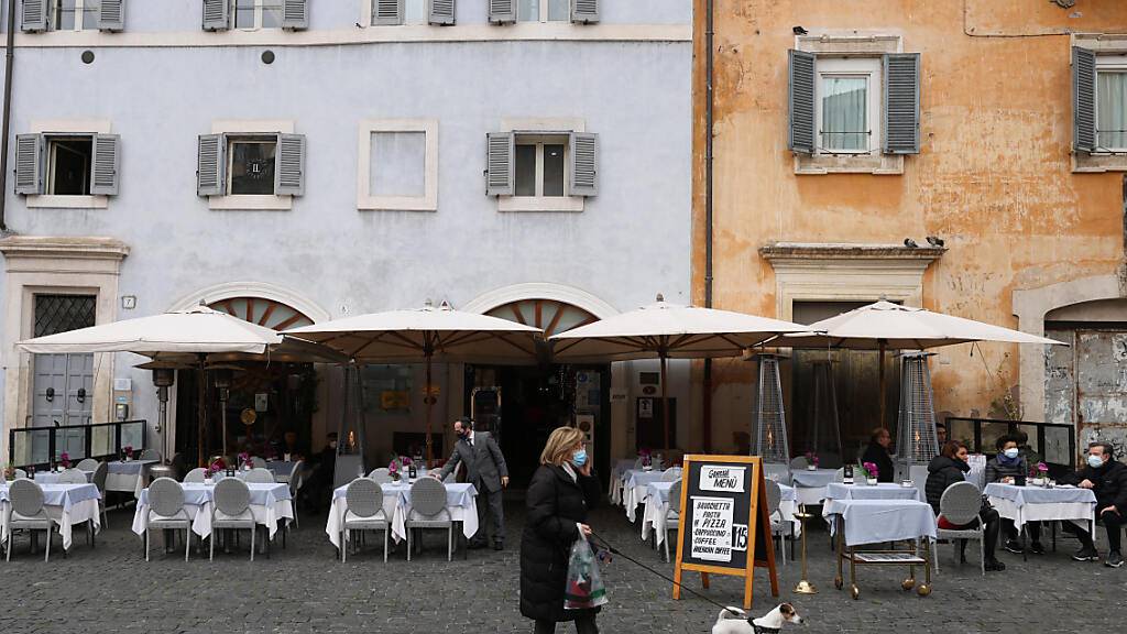 Eine Frau geht inmitten der Corona-Pandemie mit ihrem Hund an einem kürzlich wiedereröffneten Restaurant in der  Innenstadt Roms vorbei. Foto: Vincenzo Livieri/ZUMA Wire/dpa