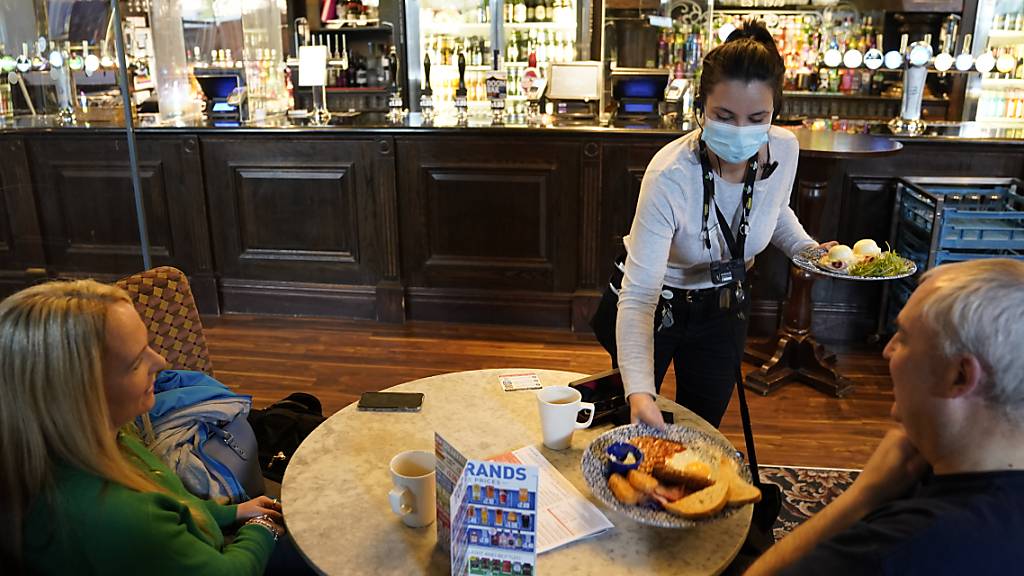 Eine Kellnerin bringt zwei Gästen einem Pub in Newcastle eine Mahlzeit an den Tisch. Die Menschen in weiten Teilen Großbritanniens haben wieder deutlich größere Freiheiten. Foto: Owen Humphreys/PA Wire/dpa