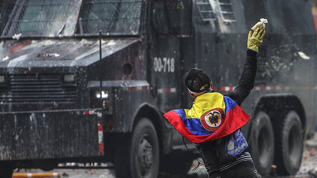 Ein wirft in einem Außenbezirk von Bogotá einen Farbbeutel auf ein Polizeifahrzeug. Foto: Ivan Valencia/AP/dpa