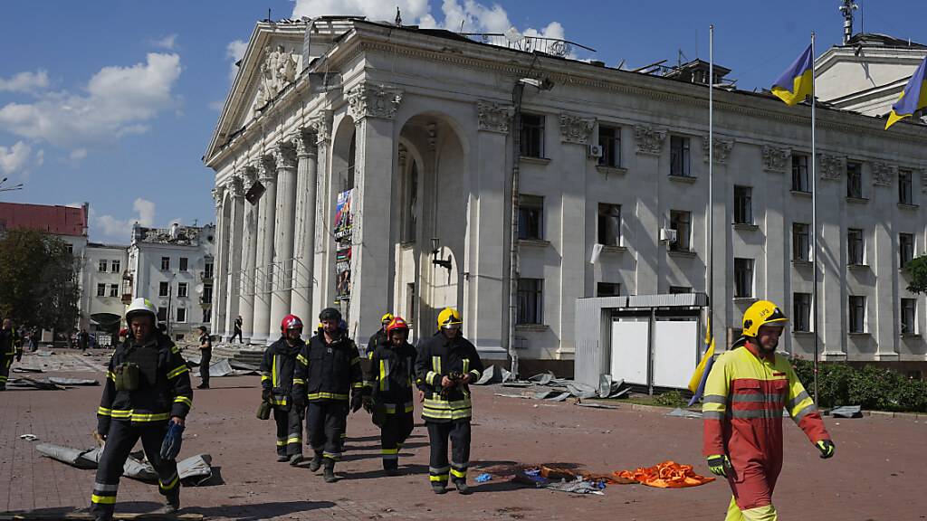 Feuerwehrleute gehen neben dem akademischen ukrainischen Musik- und Dramatheater Tschernihiw, das durch einen Angriff beschädigt wurde. Foto: Efrem Lukatsky/AP/dpa