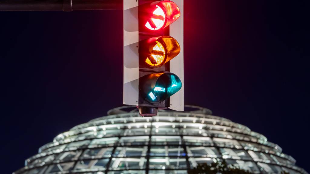 dpatopbilder - Eine Ampel vor der Kuppel des Reichstagsgebäudes leuchtet in allen drei Phasen. Einen Monat nach der Bundestagswahl steigen SPD, Grüne und FDP in die Detailverhandlungen über die Bildung einer gemeinsamen Regierung ein. Foto: Christoph Soeder/dpa