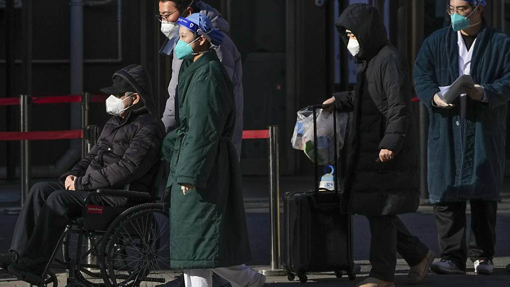 Medizinisches Personal begleitet einen älteren Patienten in einem Rollstuhl beim Verlassen einer Fieberklinik in Peking. Foto: Andy Wong/AP/dpa