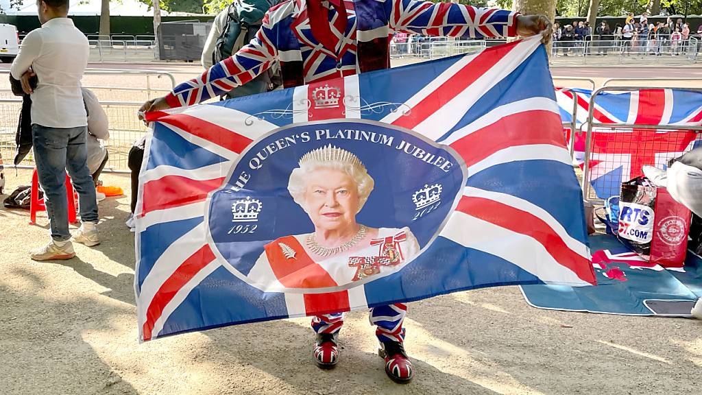 Joseph Afrane schwenkt eine Fahne mit einem Bild der Queen entlang der Pall Mall im Zentrum der Hauptstadt. Foto: Sophie Wingate/PA Wire/dpa