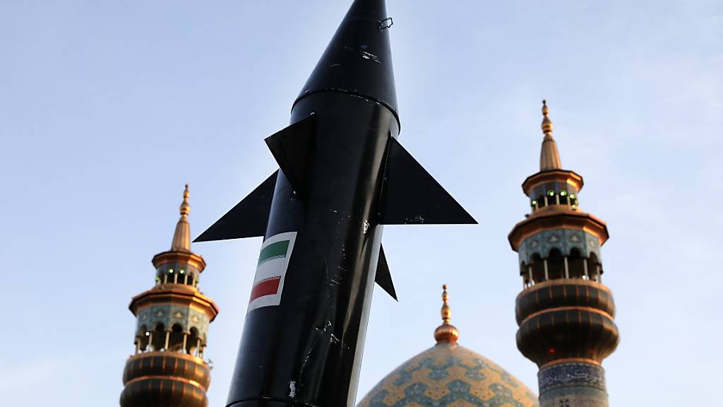Ein Modell einer Rakete wird bei einer anti-israelischen Versammlung auf dem Felestin (Palästina) Platz von iranischen Demonstranten getragen, während im Hintergrund Minarette und die Kuppel einer Moschee zu sehen sind. Foto: Vahid Salemi/AP/dpa