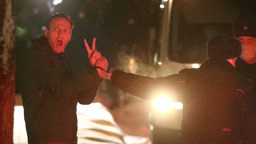 dpatopbilder - ARCHIV - Alexej Nawalny (l), Oppositionspolitiker und Kremlkritiker, macht ein V-Zeichen, während er in Handschellen von einem Polizeibeamten vor der 2. Abteilung der Direktion des russischen Innenministeriums von Chimki eskortiert wird. Foto: Sergei Bobylev/TASS/dpa