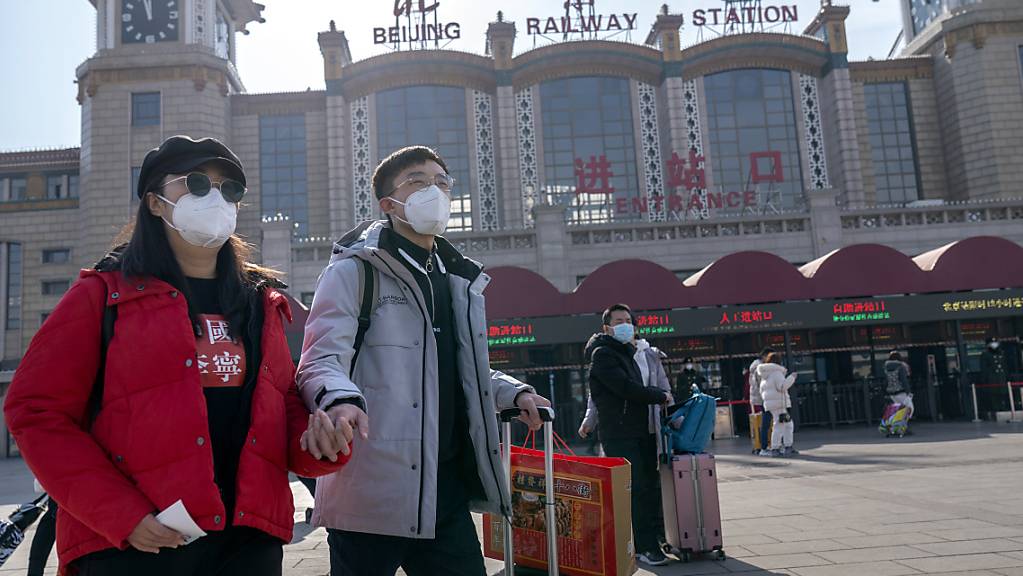 Passagiere, die als vorbeugende Maßnahme gegen die Verbreitung des Coronavirus Mund-Nasen-Bedeckungen tragen, gehen mit ihrem Gepäck vor dem Pekinger Bahnhof entlang. Foto: Mark Schiefelbein/AP/dpa