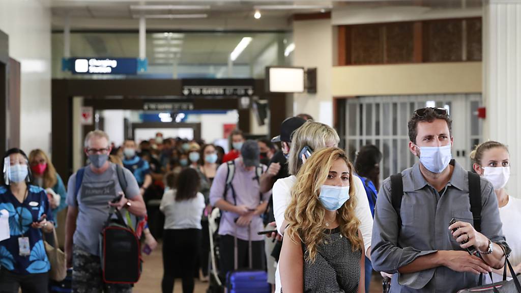 Reisende an einem Flughafen auf Hawaii tragen Mund-Nasen-Schutz. Foto: Marco Garcia/AP/dpa