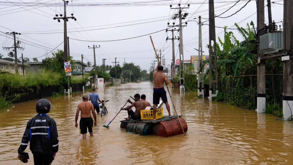 Menschen benutzen ein provisorisches Floß, um auf einer überfluteten Straße zu fahren. Foto: Eranga Jayawardena/AP/dpa