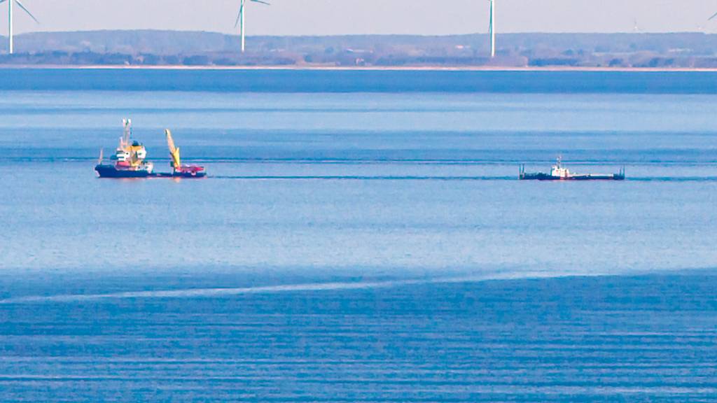 dpatopbilder - Ein Schiff zieht vor Fehmarn die Barge mit dem gestrandetem Wal. Im Hintergrund ist die dänische Küste zu sehen. Foto: Bodo Marks/dpa