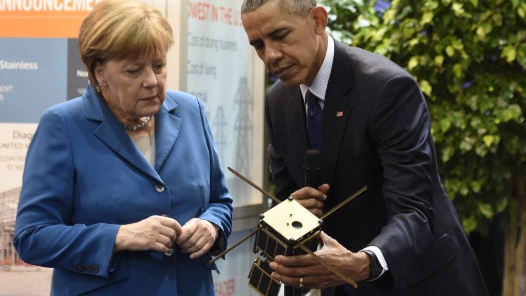 Merkel und Obama betrachten an der Messe einen kleinen Satelliten.
