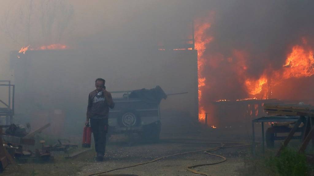 Ein Mann trägt einen Feuerlöscher in der Hand und telefoniert, während eine Lagerhalle brennt. Foto: Bruno Fonseca/AP