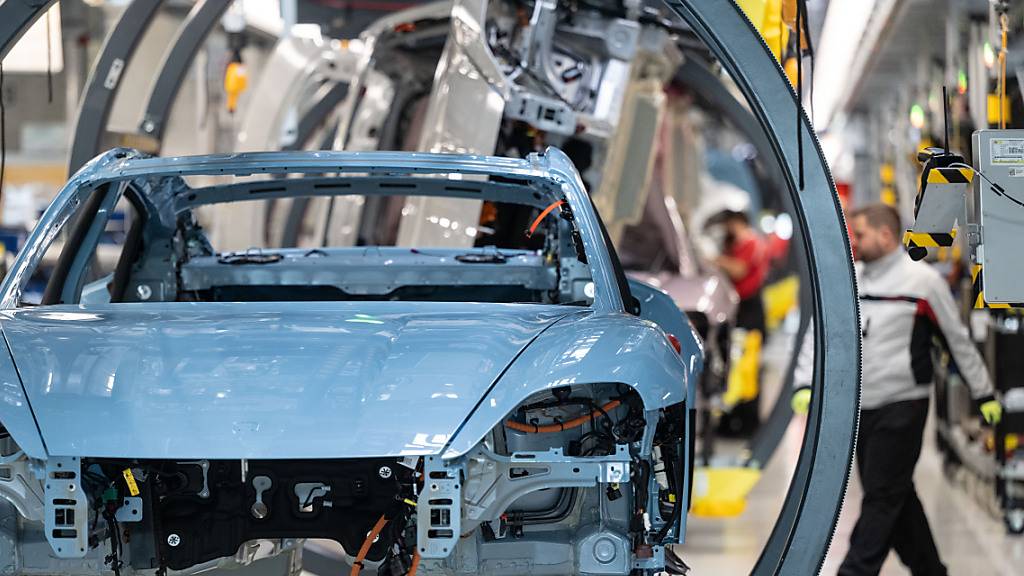 Ein Mitarbeiter von Porsche montiert in einer Produktionshalle des Porsche-Stammwerks einen Porsche Taycan (Archivbild).