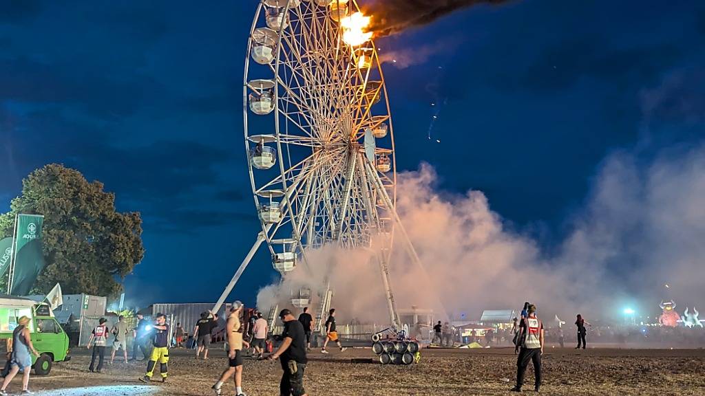 dpatopbilder - Besucher des Highfield-Festivals und Helfer blicken auf ein Riesenrad, an dem Flammen zu sehen sind. Auf dem Highfield-Festival am Störmthaler See ist ein Feuer an einem Riesenrad ausgebrochen. Es gab rund 30 Verletzte. Foto: -/spm-gruppe/dpa