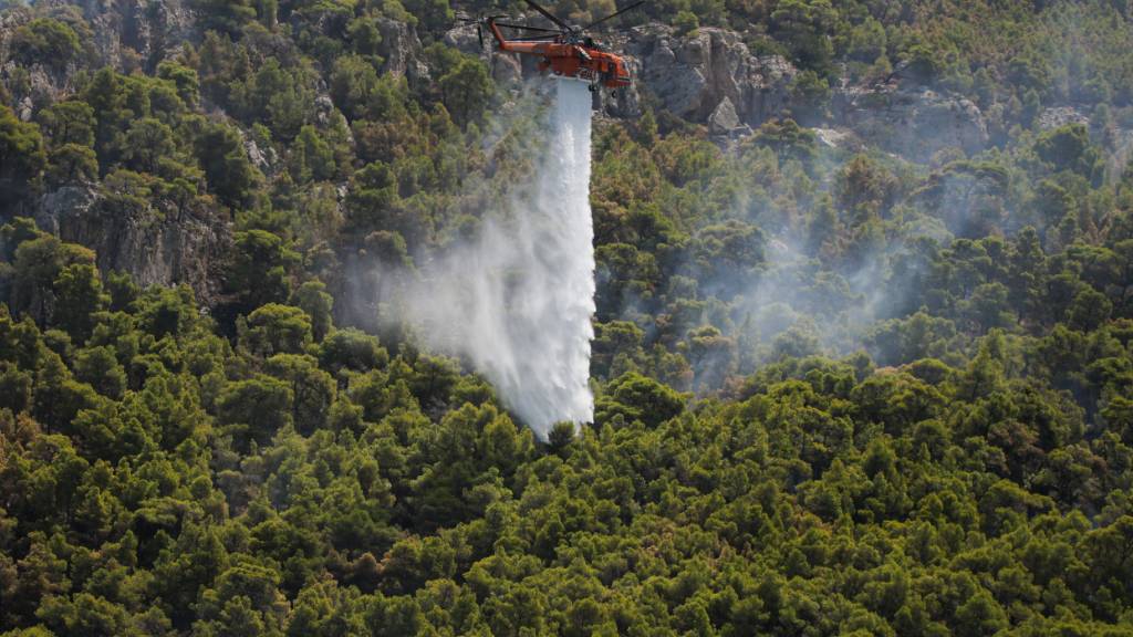 ARCHIV - Ein Löschhubschrauber wirft in Griechenland Wasser über einem Wald ab. Foto: Socrates Baltagiannis/dpa/Archivbild