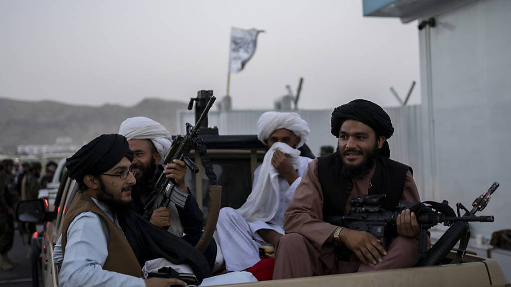Taliban-Kämpfer sitzen auf der Ladefläche eines Autos auf dem Gelände des Flughafens in Kabul und halten Waffen in ihren Händen. Foto: Bernat Armangue/AP/dpa