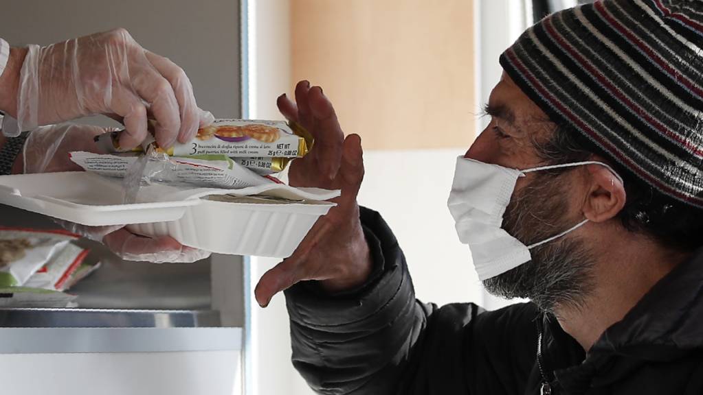 Ein Freiwilliger reicht einem Obdachlosen mit Mund-Nasen-Schutz Essen. Landesweit in Italien sind verschärfte Corona-Schutzvorschriften in Kraft getreten.