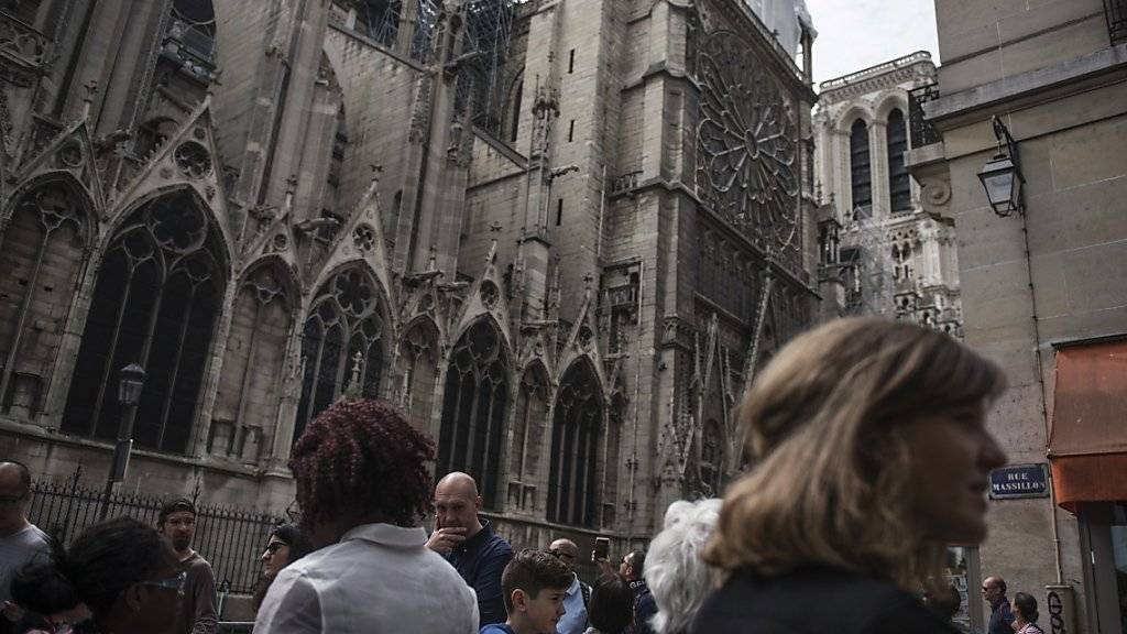 Touristen sehen sich gut eine Woche nach dem verheerenden Brand den Schaden an der Kathedrale Notre-Dame an.  Am Dienstag wurde begonnen, eine Plane auf der mehr als 850 Jahre alten Kathedrale anzubringen, deren Dach in grossen Teilen zerstört wurde. (Archivbild)