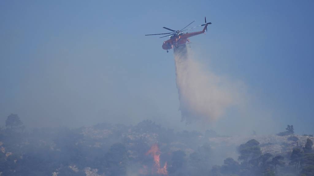 Ein Hubschrauber wirft Wasser über einem Waldbrand auf dem Berg Parnitha ab. Foto: Thanassis Stavrakis/AP/dpa